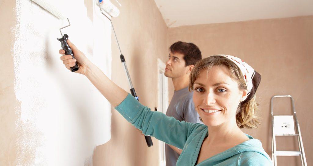 Couple using paint rollers on the wall of a living room