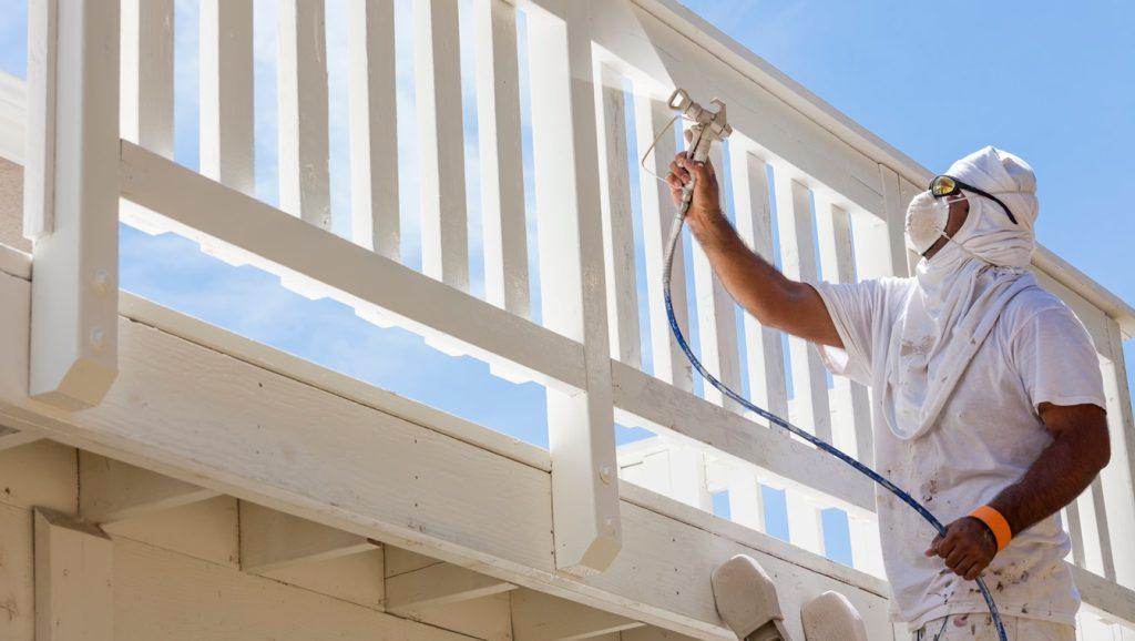 House painter wearing facial protection spray painting a deck