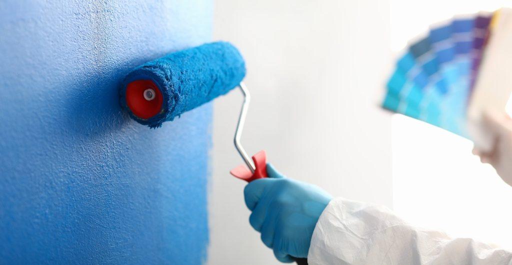 Person painting a wall with a roller, holding a colourful palette