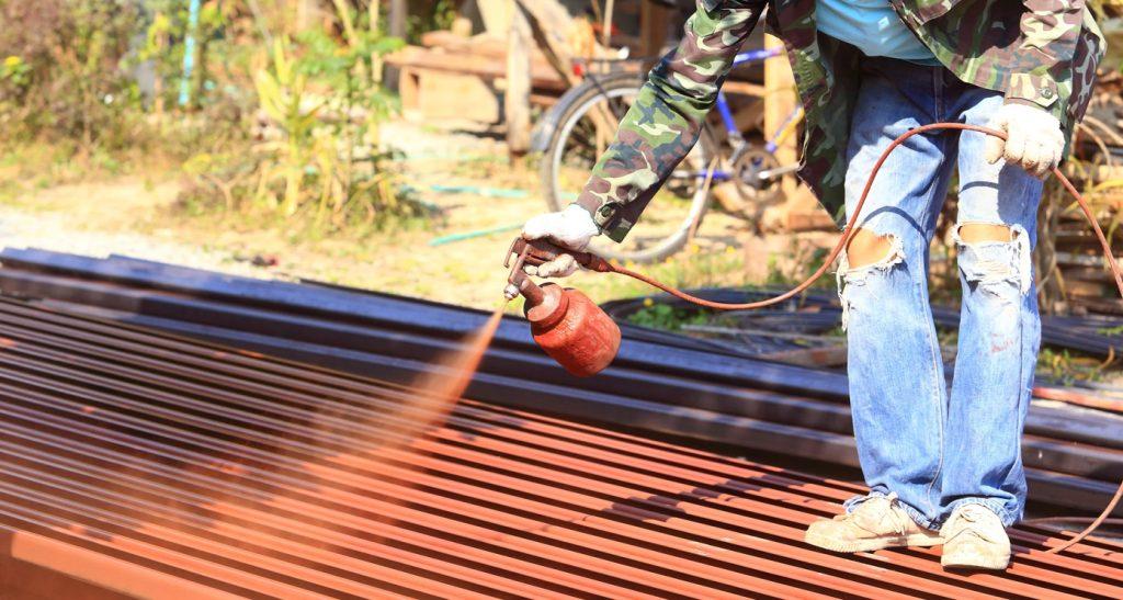 Worker spray-painting red colour on roof steel for house construction