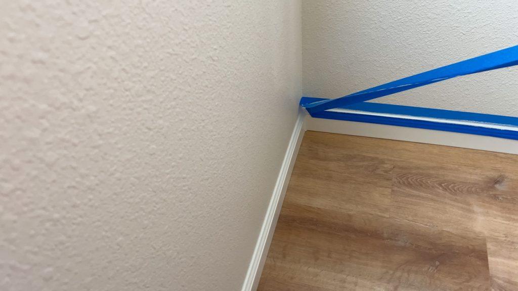 A corner section of a room with painter's tape applied along the baseboard and adjacent walls