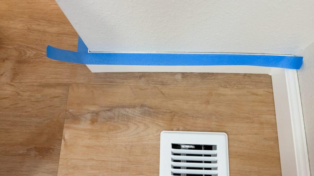 Blue painter tape neatly applied along baseboards and a corner wall junction above a wood floor