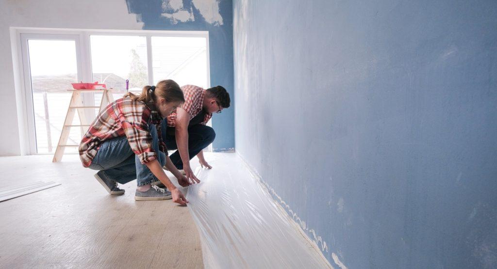Couple renovating a new house apartment, putting protective film on the floor