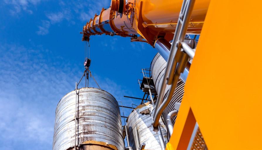 Crane carry a heavy metal silo in industrial complex