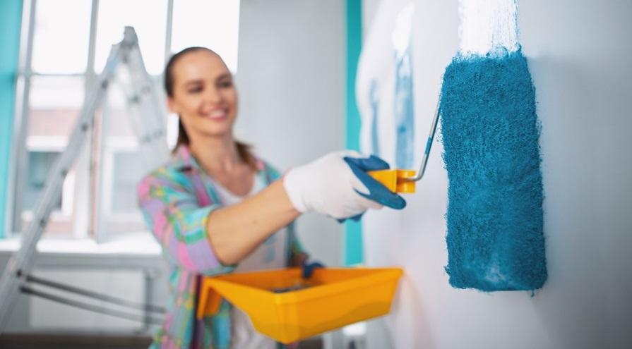 Delighted young woman holding a roller and painting the walls