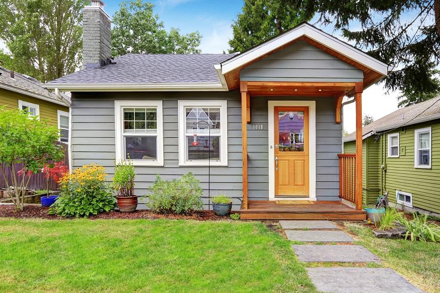 Small grey house with wooden deck, front yard with flower bed and lawn