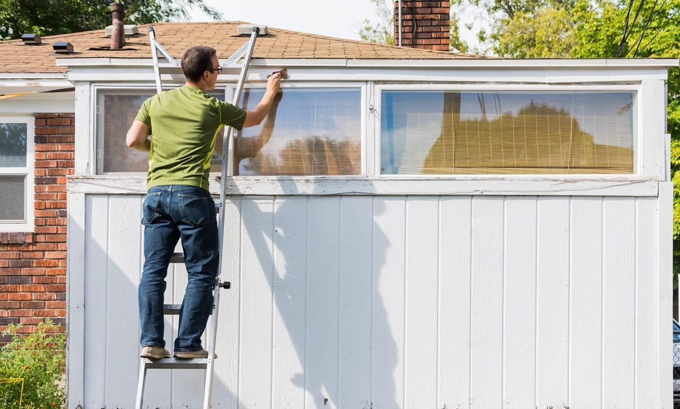 Male paints white trim of old urban home