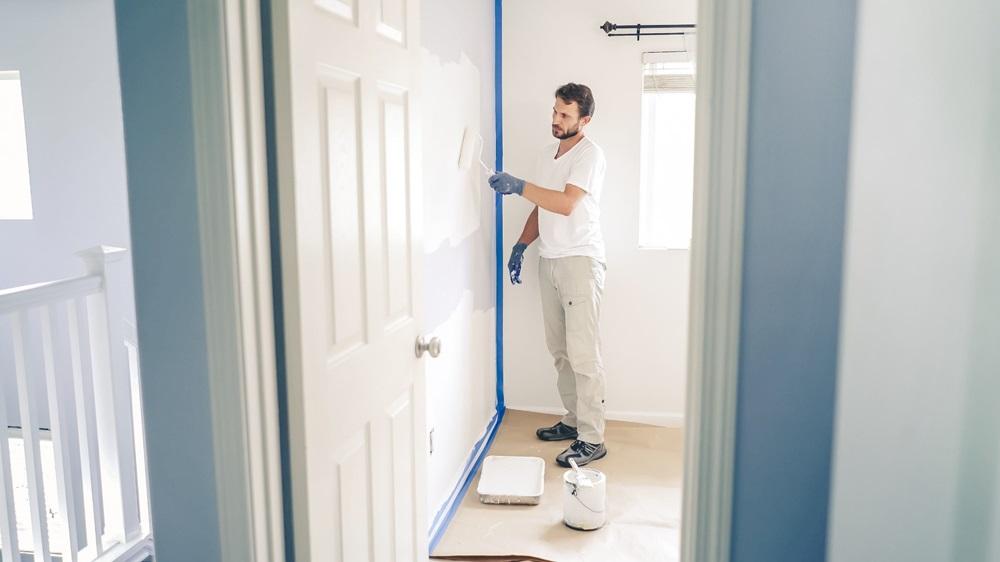 Painter man painting the wall in home with paint roller and white color