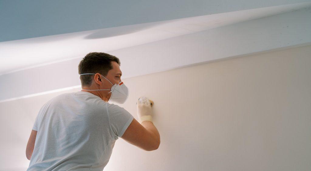 Specialist in a mask and gloves treats the wall for mould and fungus