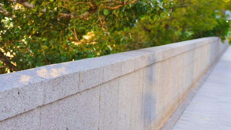 Stone gray fence in the park, gray wall in thickets