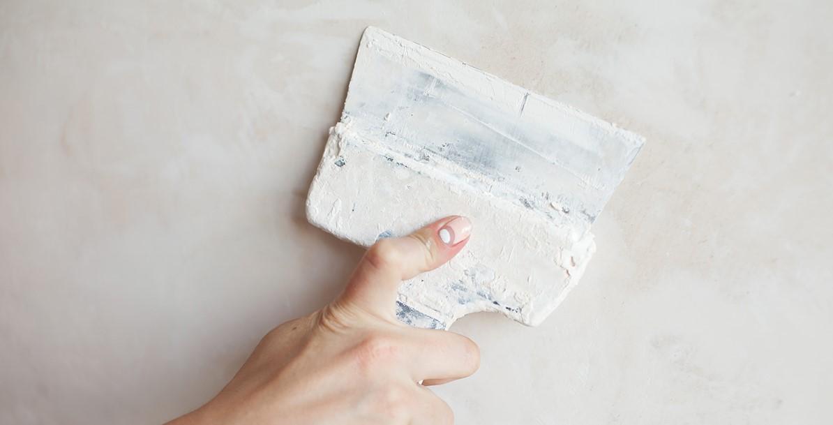 Woman hand with palette knife or scraper and cement filling for house renovation