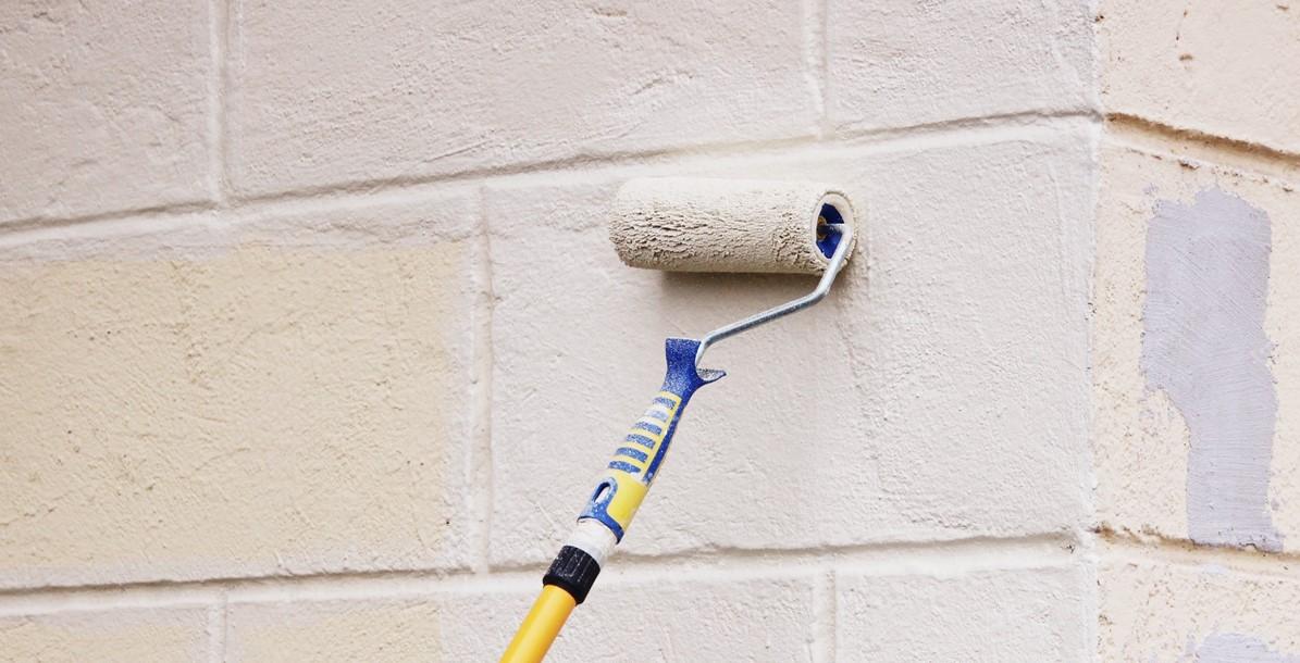 Worker man painter paints the wall with beige paint with a roller
