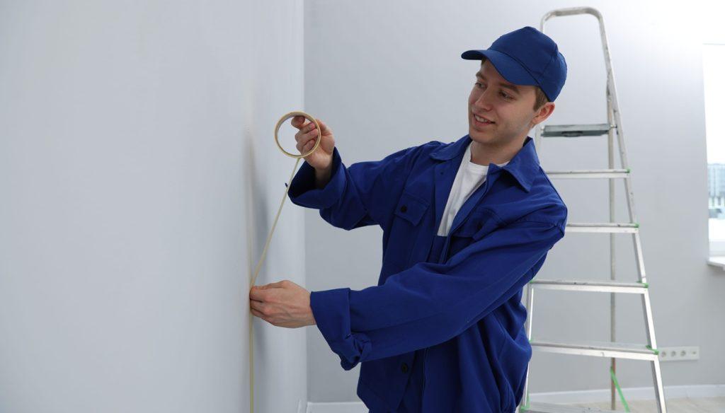Worker putting painter's tape on wall in room