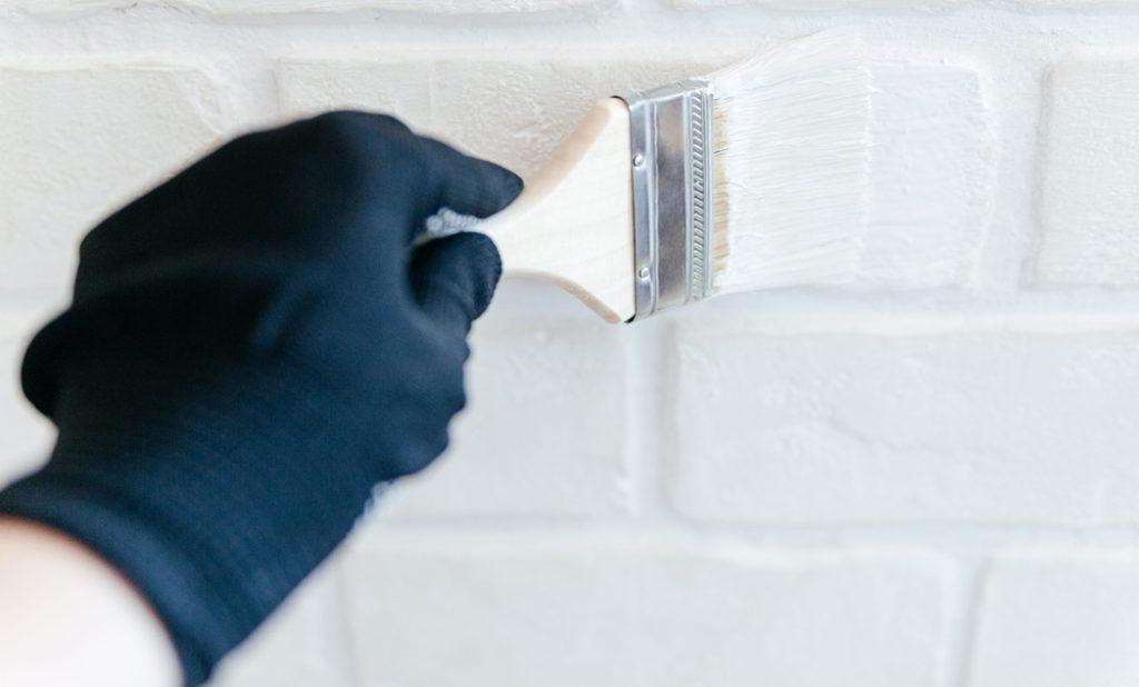 Worker's hand with a brush painting a brick wall with white paint